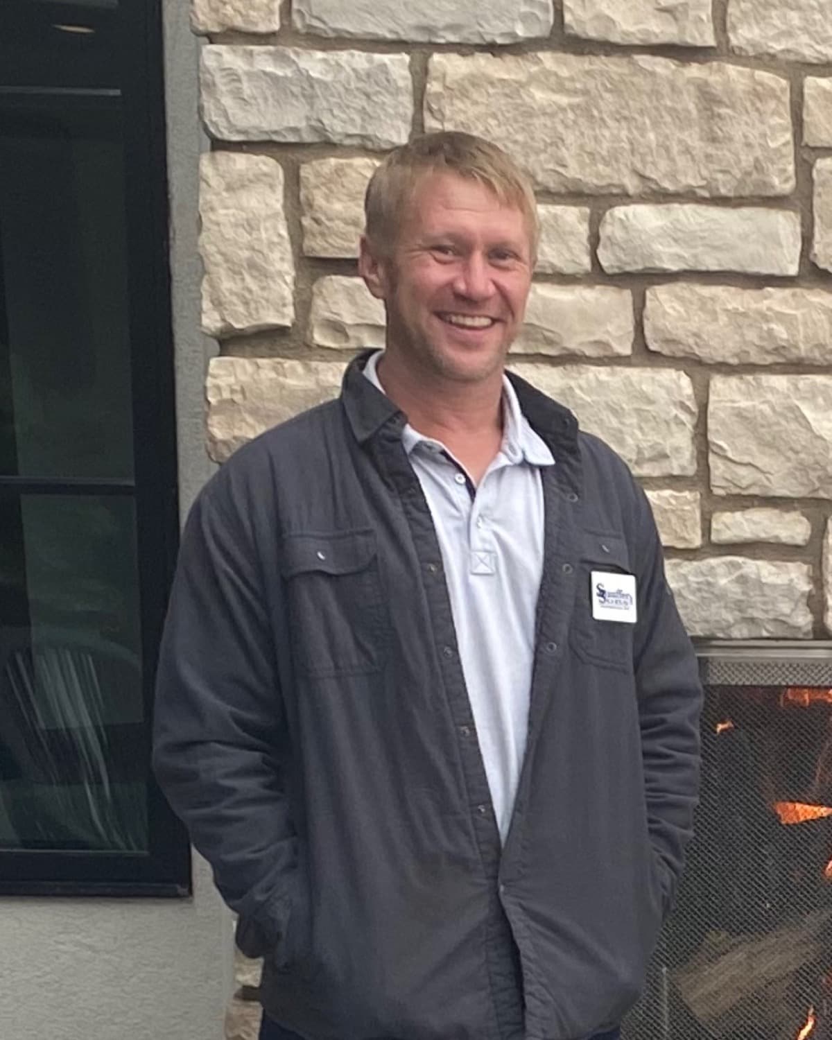 Bryce Harmon in a Stauffer & Sons work shirt, standing beside a stone fireplace on a job site