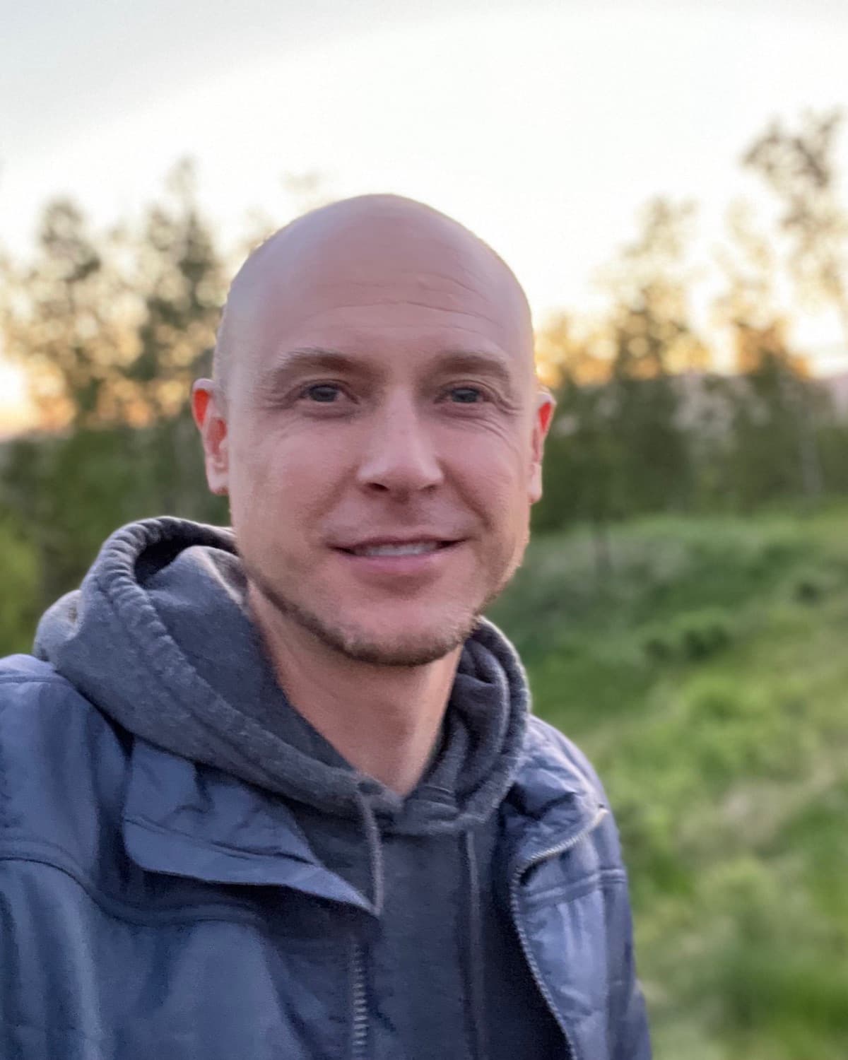 Sam Friesema outdoors at dusk with trees and a hillside behind him