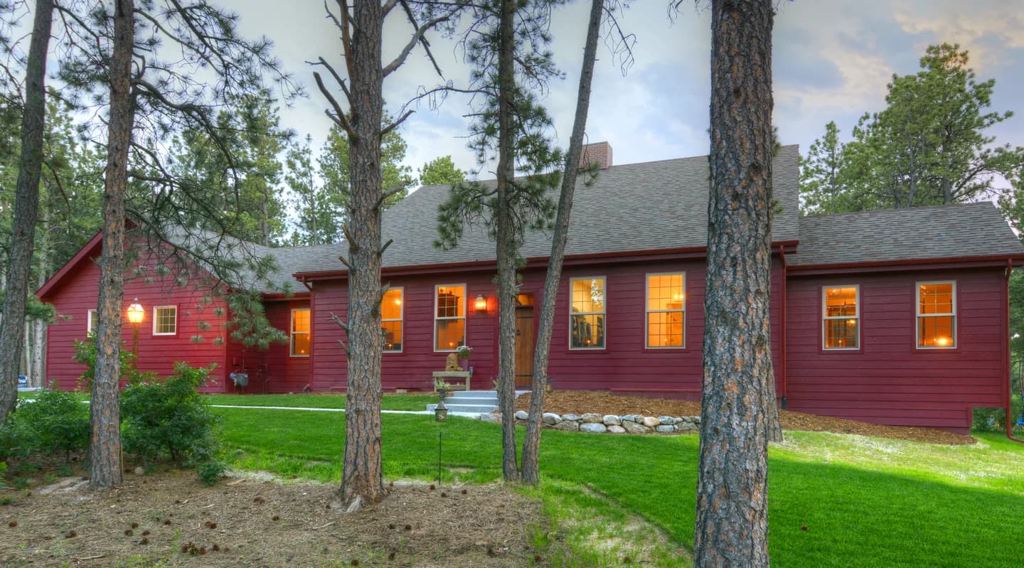 Front elevation of a red lap-siding custom home glowing at twilight among tall ponderosa pines