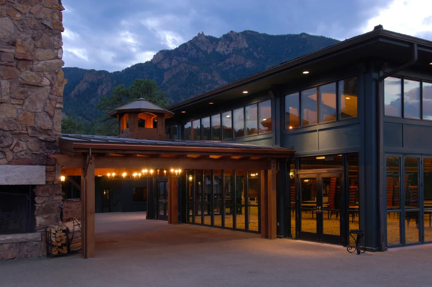 Renovated lodge exterior at twilight with folding glass walls, string-lit terrace and mountain backdrop