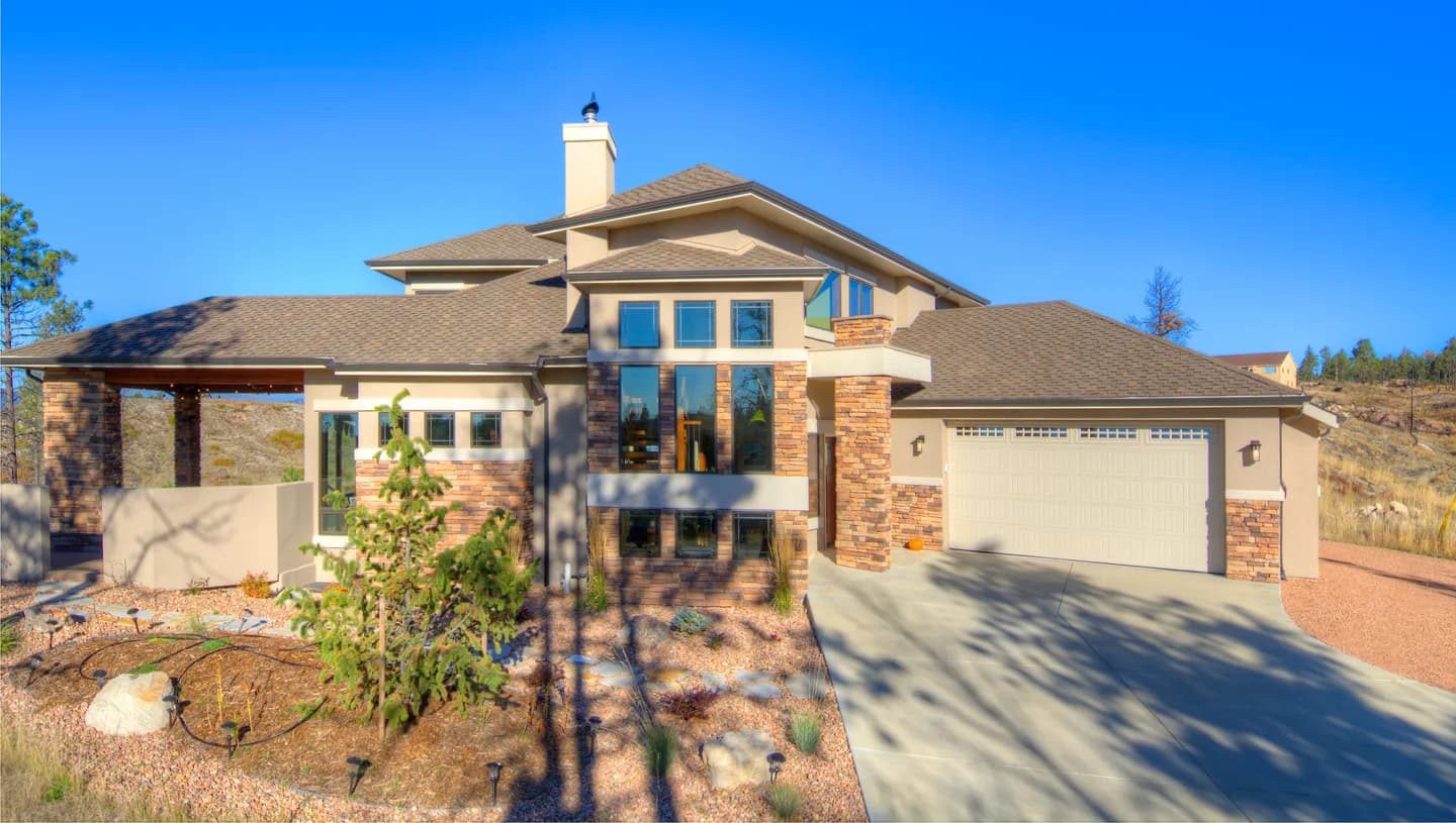 Contemporary prairie-style custom home with stucco, stone columns and deep overhangs under blue sky.