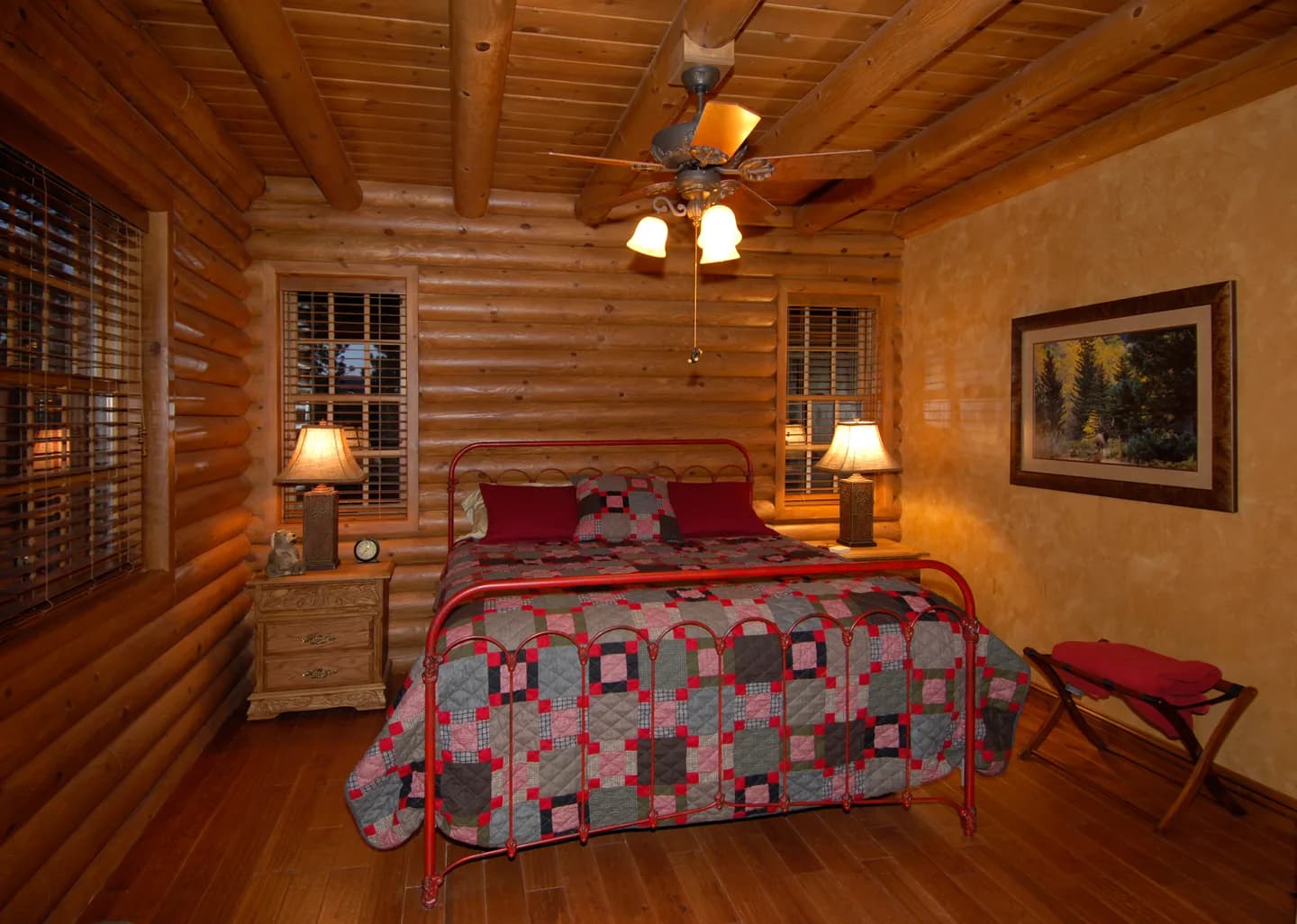 Guest bedroom in a log home with iron bed, patchwork quilt, log walls and exposed log ceiling beams