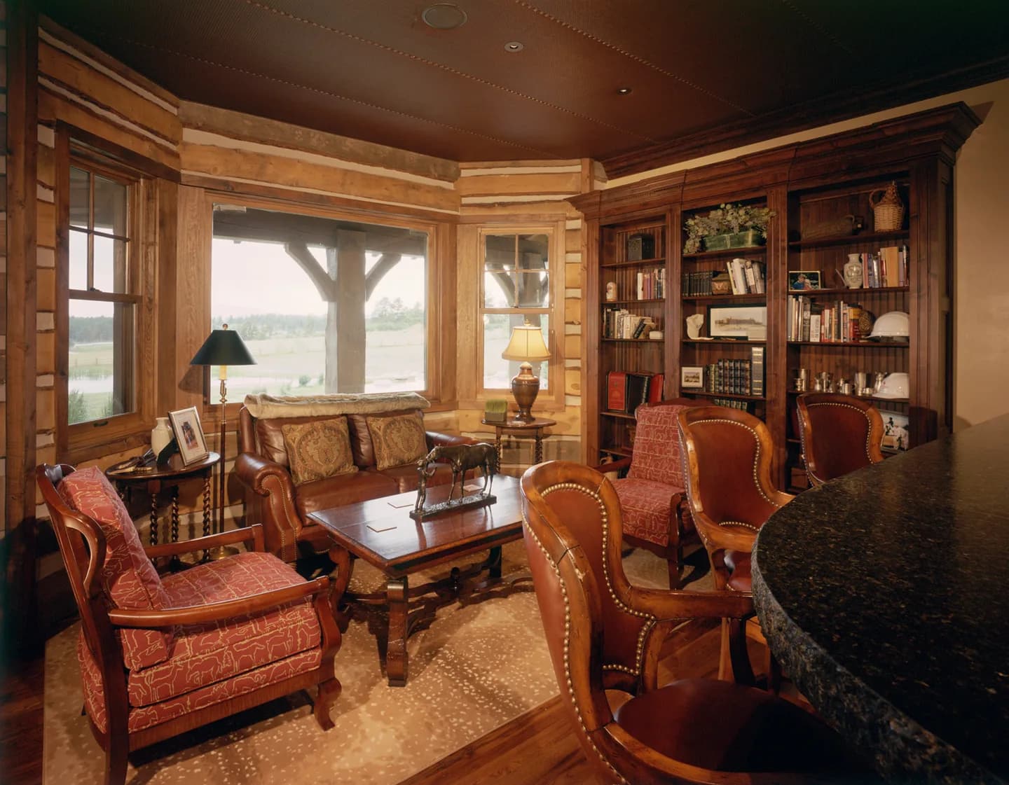 Home bar and library with granite counter, floor-to-ceiling built-in bookcases and log walls under a coffered ceiling