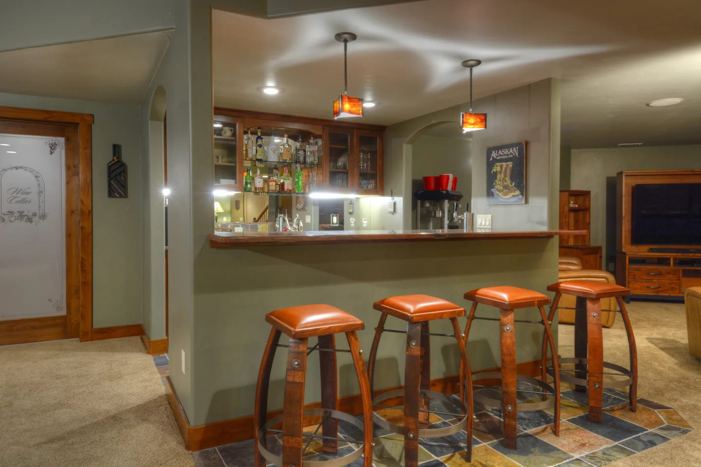 Basement wet bar with glass-front cabinets, back-lit shelving and barrel-stave bar stools.
