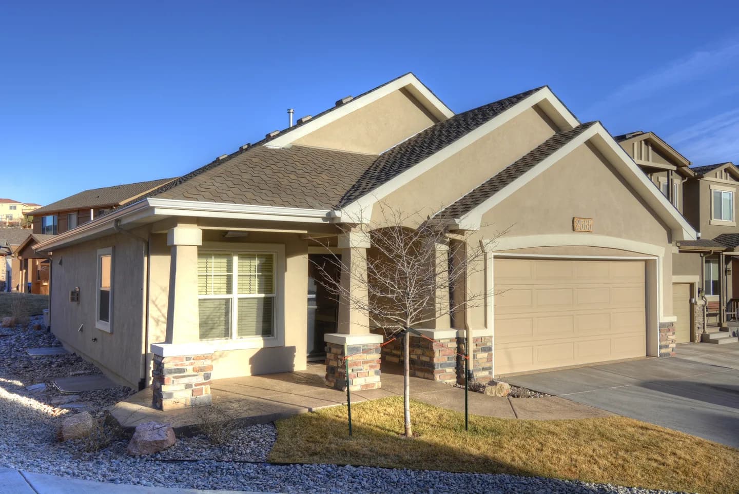 Single-level stucco patio home with stone columns, covered front porch and two-car garage.