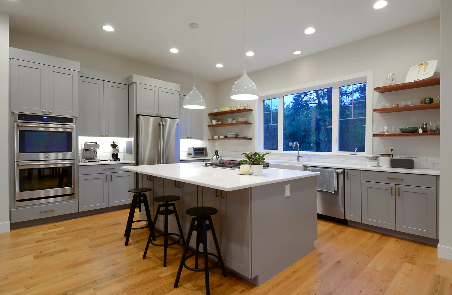 Bright kitchen with gray shaker cabinets, quartz island, open walnut shelving and stainless double ovens