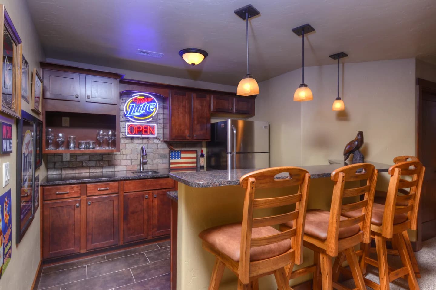 Lower-level wet bar with cherry cabinets, granite counter, tile backsplash and bar stool seating.