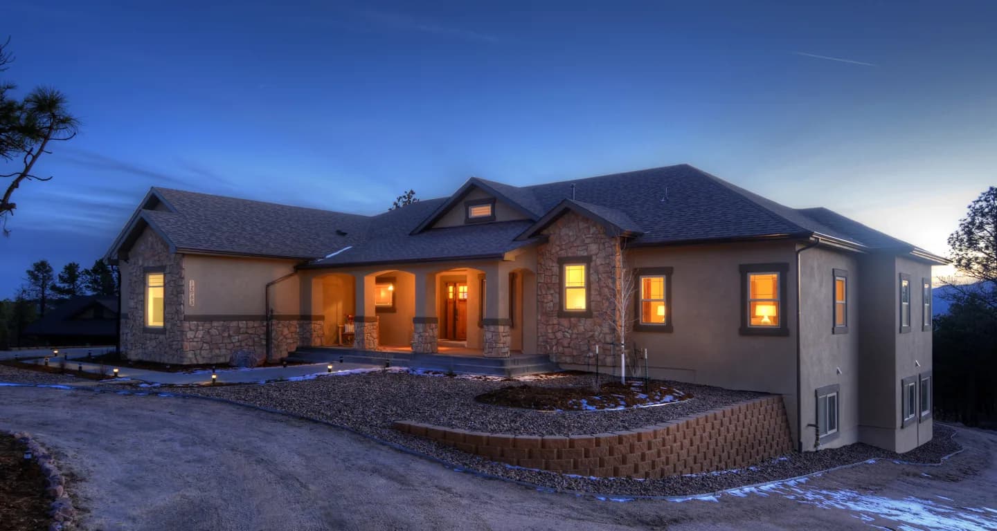 Craftsman ranch custom home glowing at twilight with stone accents and terraced retaining walls.