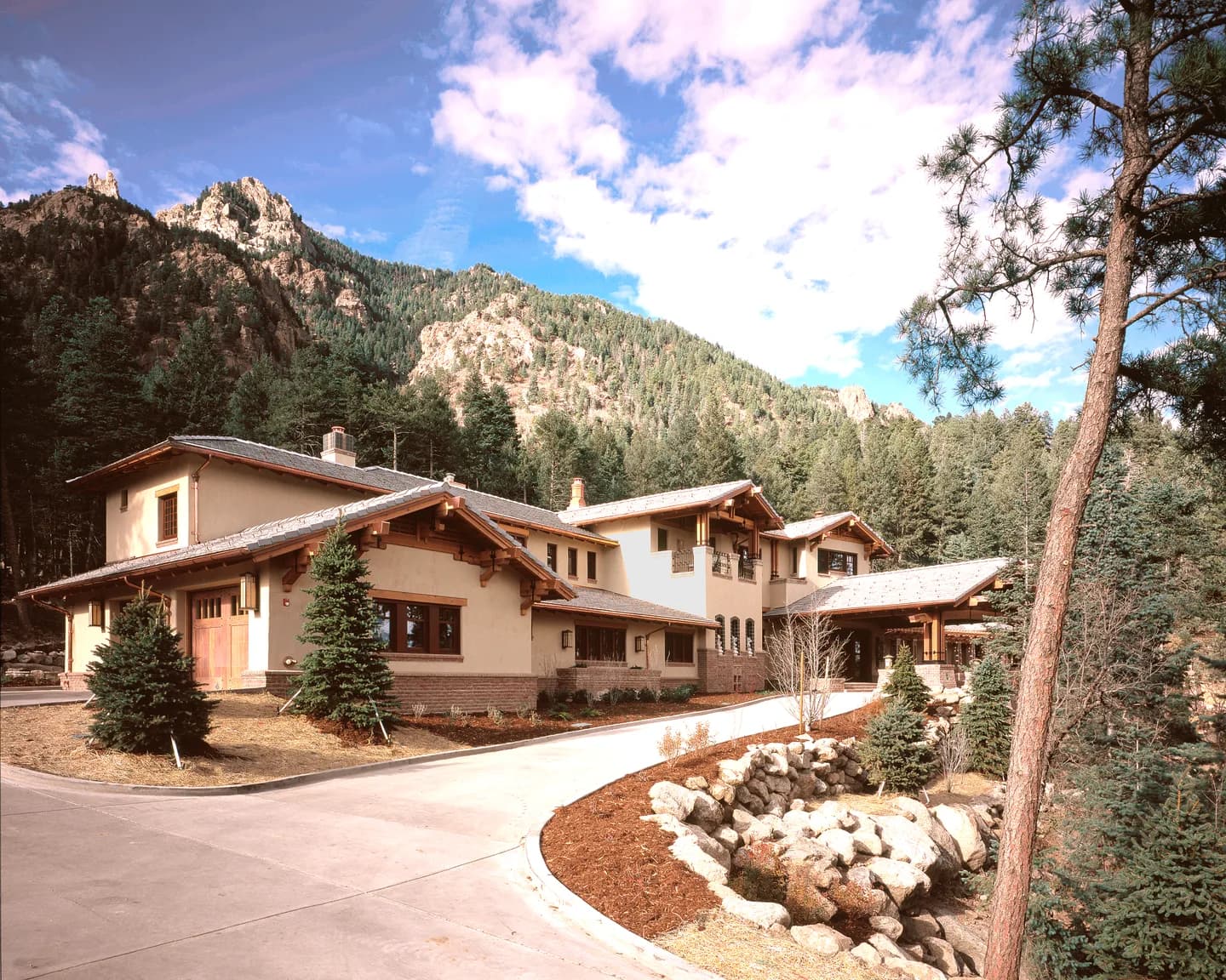 Craftsman-style mountain estate with timber brackets and brick base below a rocky pine-covered ridge