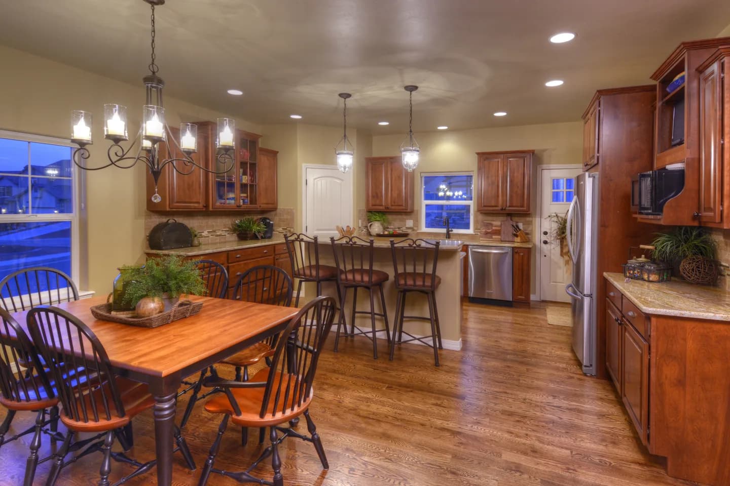 Dining area with wrought iron chandelier and Windsor chairs open to the kitchen and island seating.