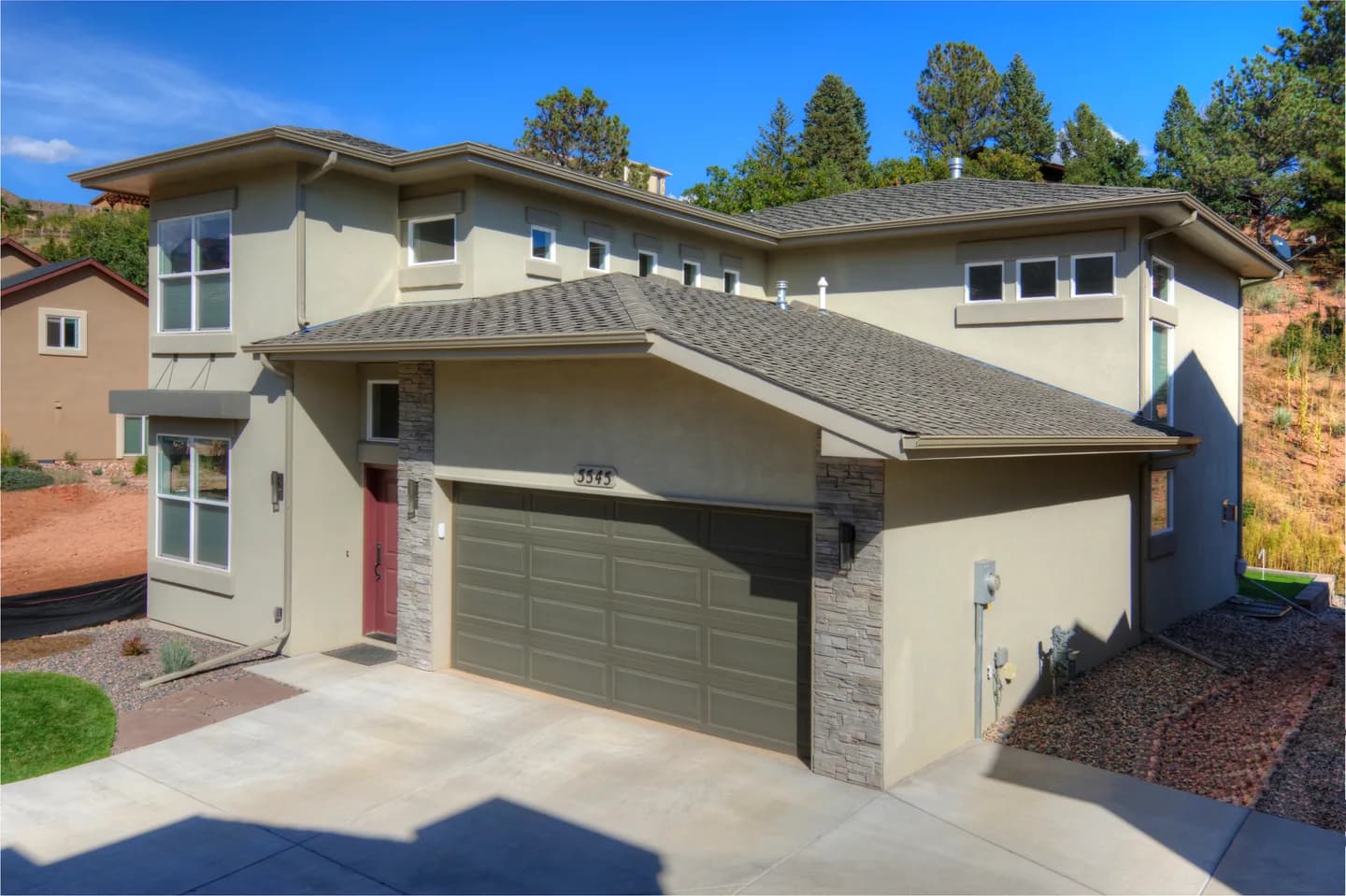 Contemporary two-story stucco home with stone-wrapped garage and low-pitch overlapping rooflines.
