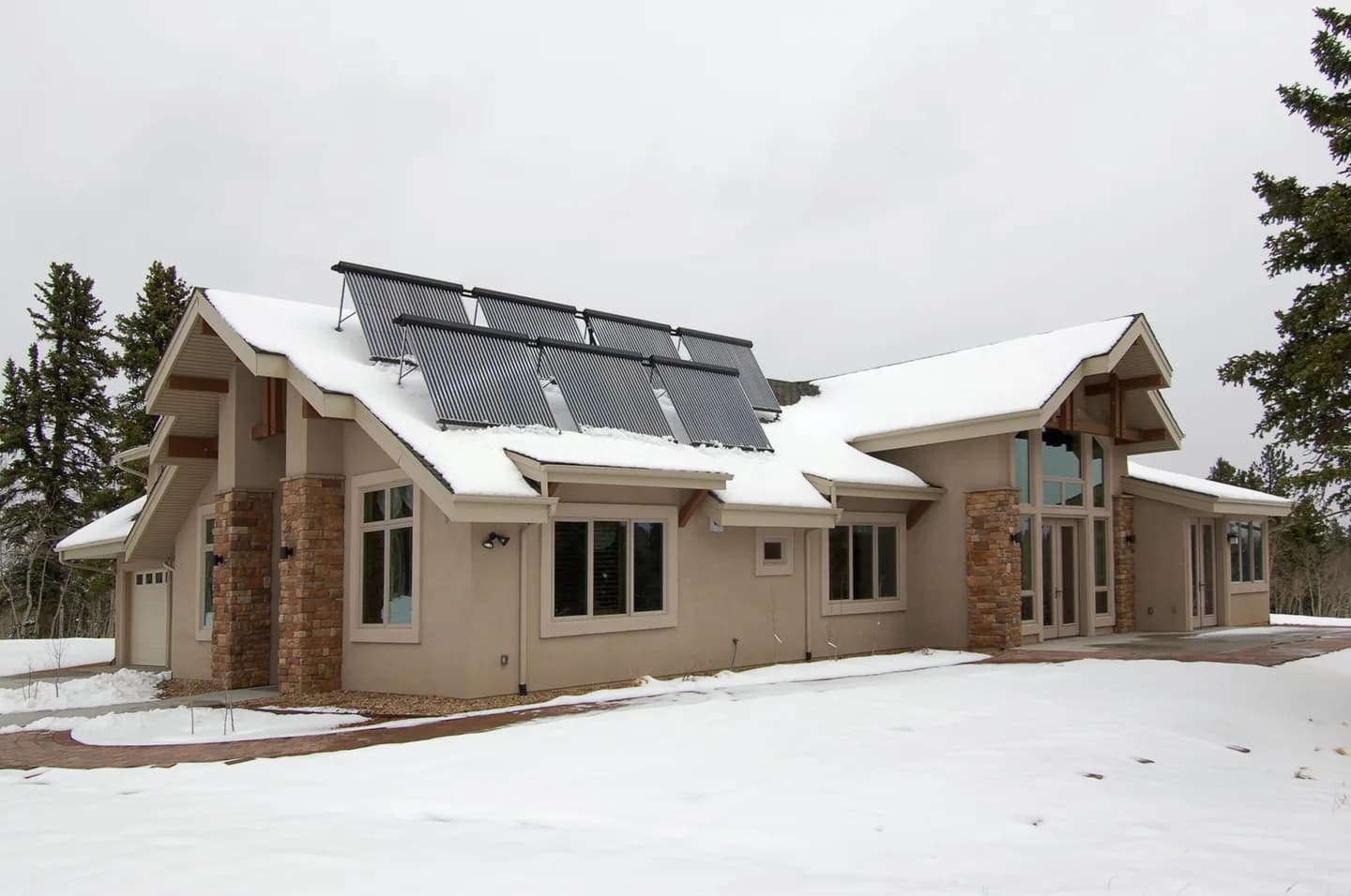 Mountain home exterior in snow with roof-mounted solar thermal collectors, stucco siding and stone-veneer columns